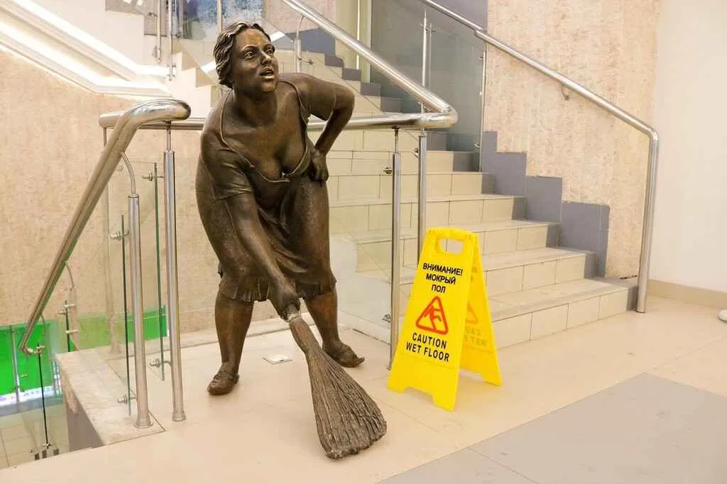 The sculpture of the cleaning lady is located on the stairs of a shopping center